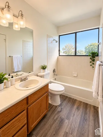 Wood-finish flooring, single vanity with wood cabinetry, and a full-size bathtub with tiled surround
