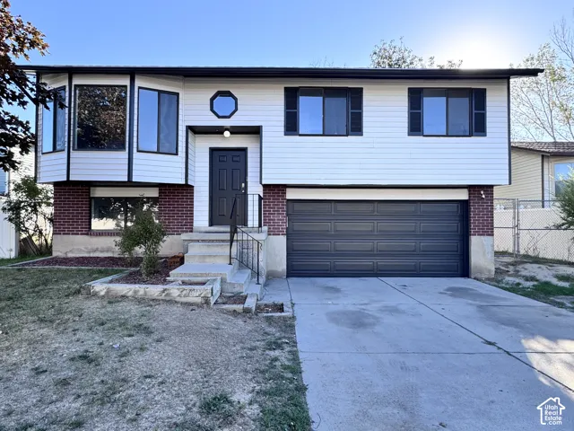 Split-level residence featuring a two-car garage, brick and siding exterior, large bay window, concrete driveway, and front entry steps with handrail
