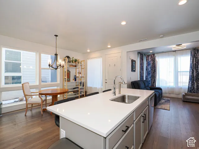 Expansive wood-finish flooring throughout, featuring a kitchen island with a built-in sink and white countertop, recessed lighting, and a dining area with a chandelier