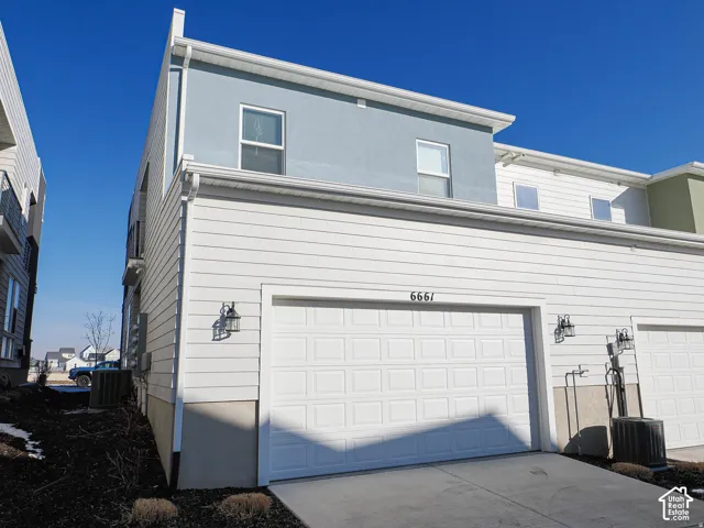 Two-car garage with panel doors, exterior wall lanterns, and a textured stucco facade on the upper level