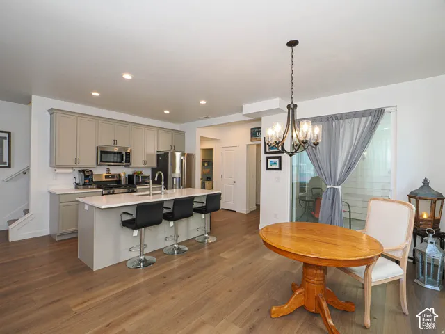 Kitchen featuring gray cabinetry, stainless steel appliances, a white countertop island with seating, and wood-finish flooring
