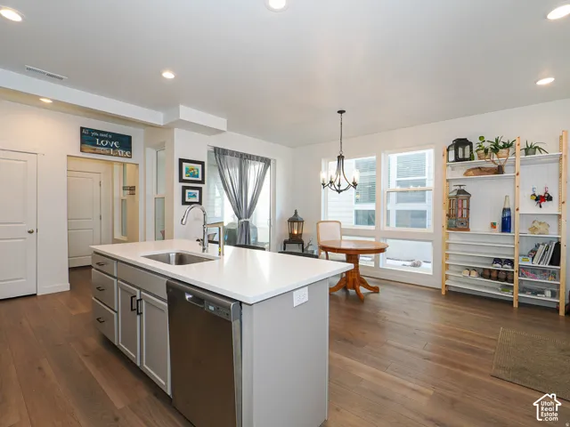 Kitchen island with a stainless steel sink and appliances, white countertops, wood-finish flooring, and recessed lighting