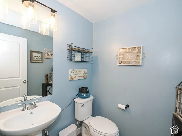 Pedestal sink with chrome faucet, wall-mounted mirror, and overhead vanity light