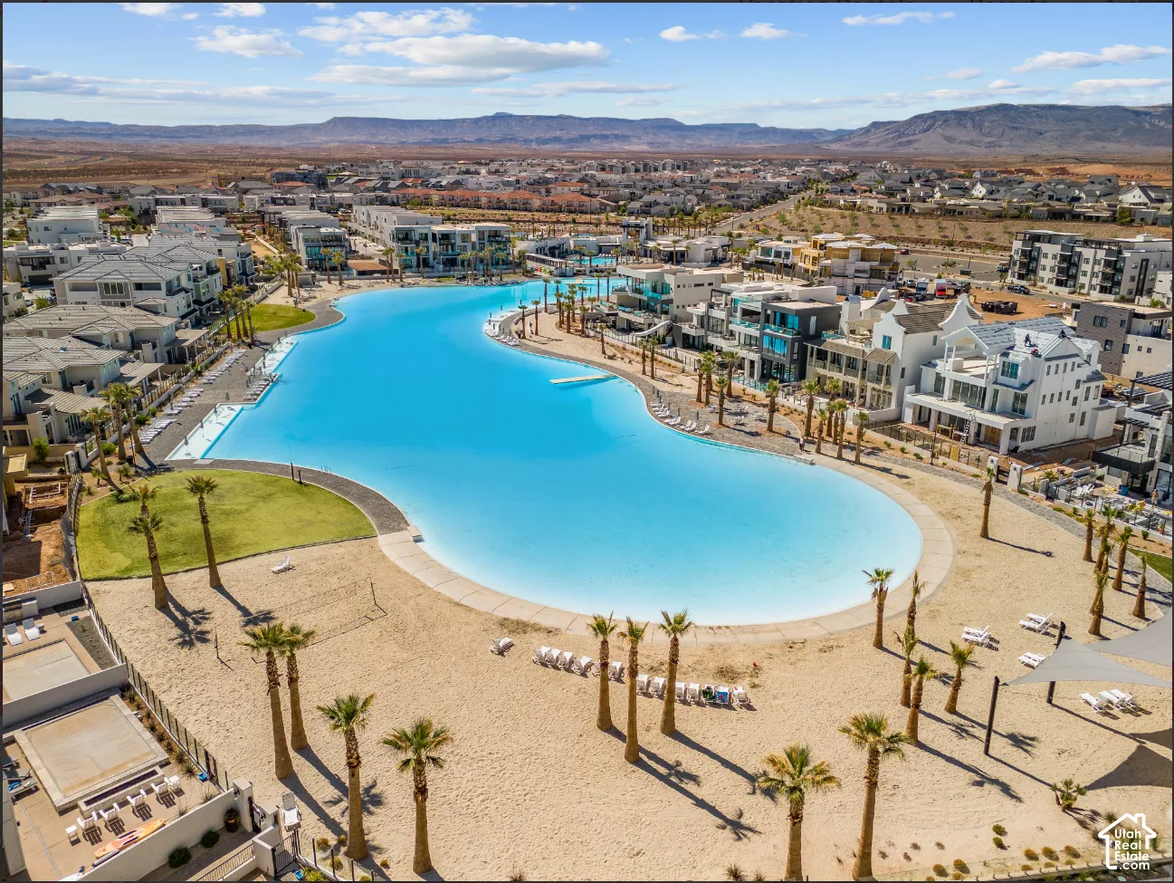 Expansive lagoon with surrounding sandy beach, lush green spaces, and mature palm trees