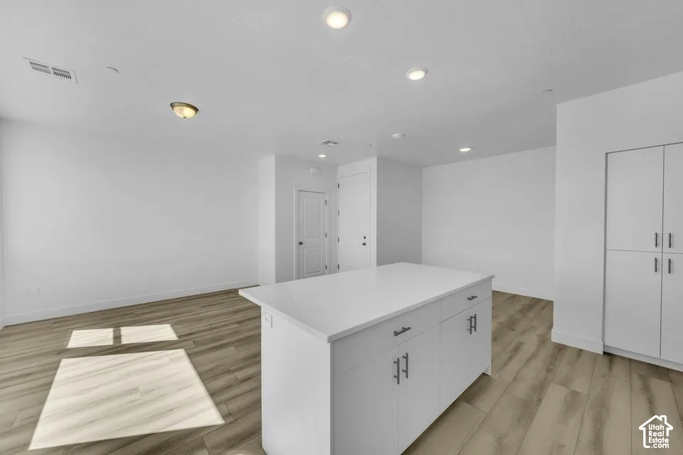 Central kitchen island with a light-toned countertop, wood-finish flooring, recessed lighting, and white cabinetry