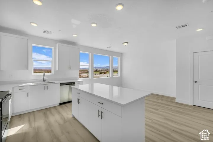 Kitchen featuring white cabinetry, a large kitchen island with a white countertop, wood-finish flooring, and multiple windows