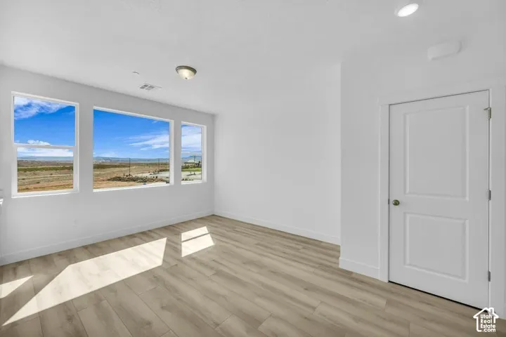 Multiple large windows, light wood-finish flooring, recessed lighting, and a white paneled door
