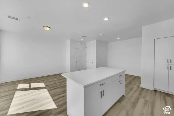 Central kitchen island with a light-toned countertop, wood-finish flooring, recessed lighting, and white cabinetry