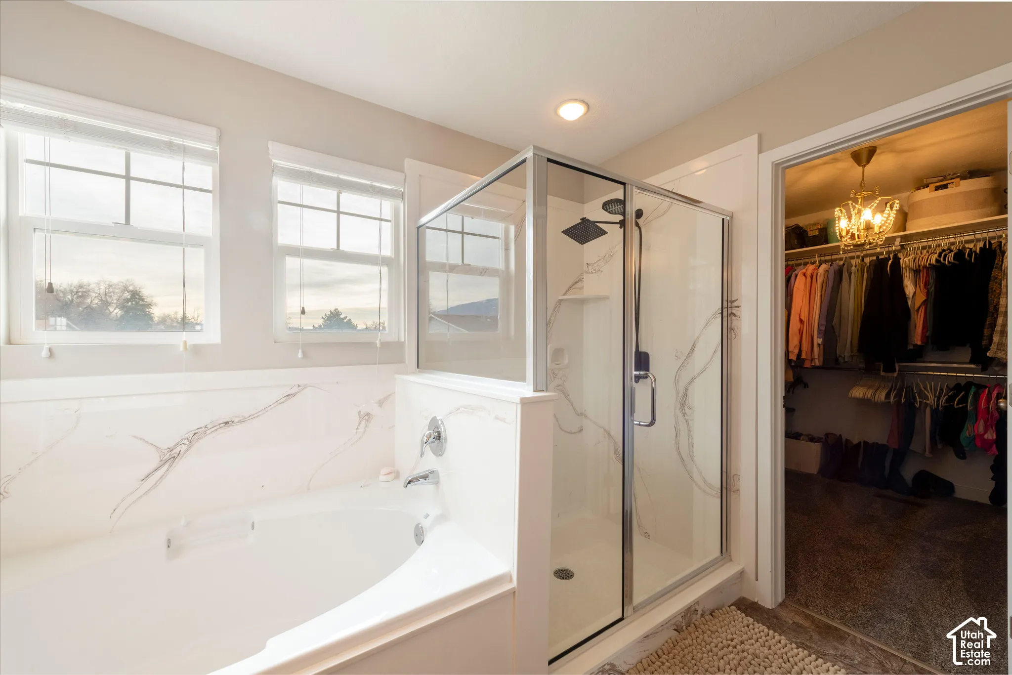 Soaking tub with a polished chrome faucet, glass-enclosed shower with a matte black rainfall showerhead, and a walk-in closet featuring built-in shelving