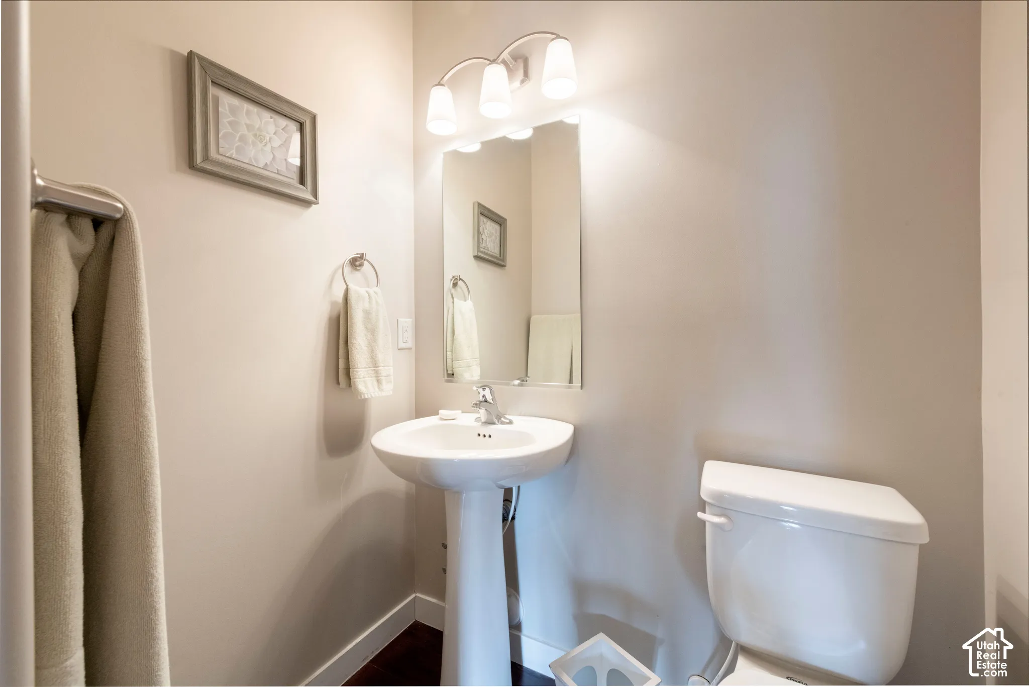 Pedestal sink with chrome faucet, wall-mounted mirror, and overhead vanity lighting