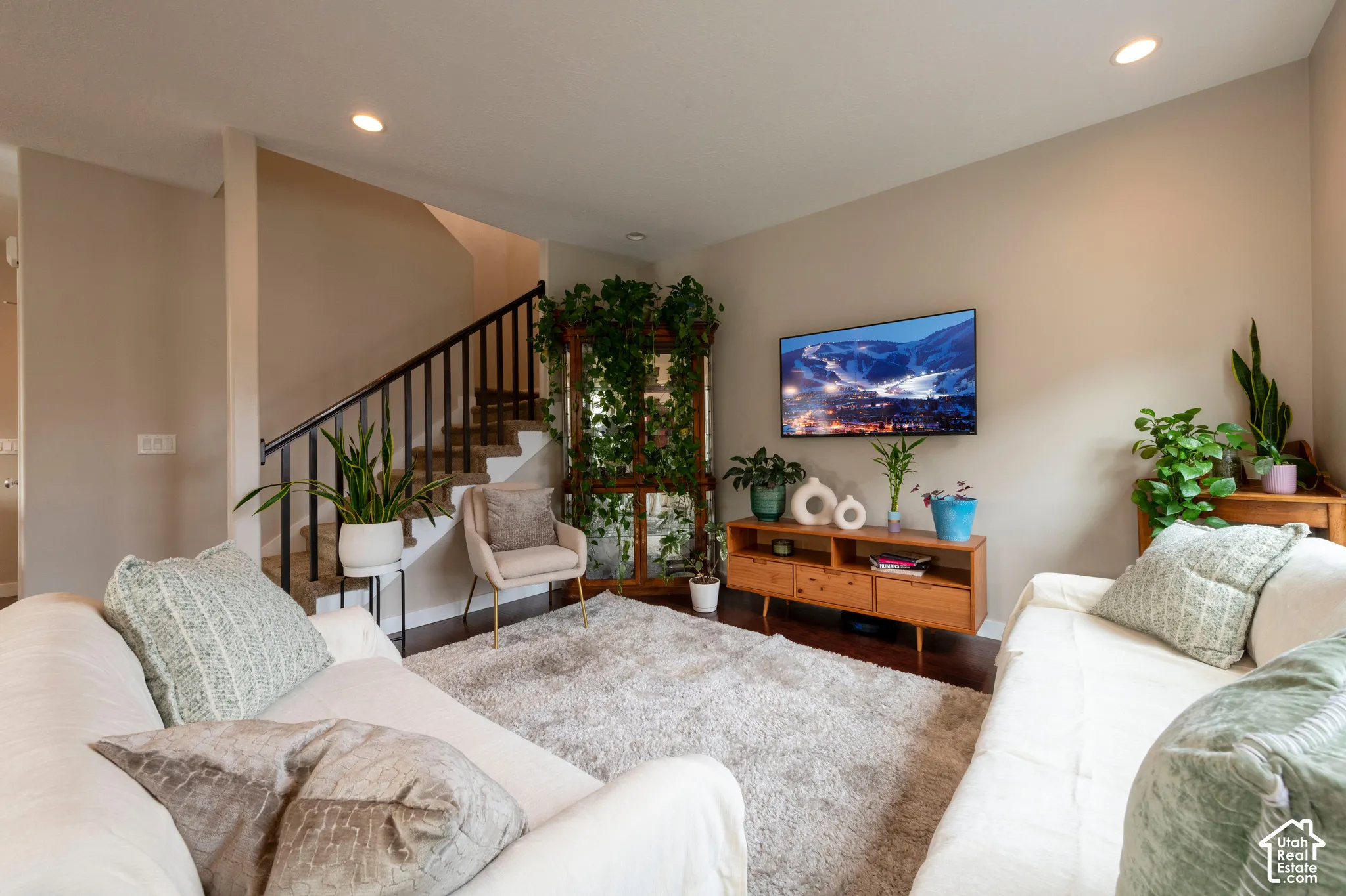Recessed lighting illuminates the living space featuring wood-finish flooring and a staircase with a black metal railing