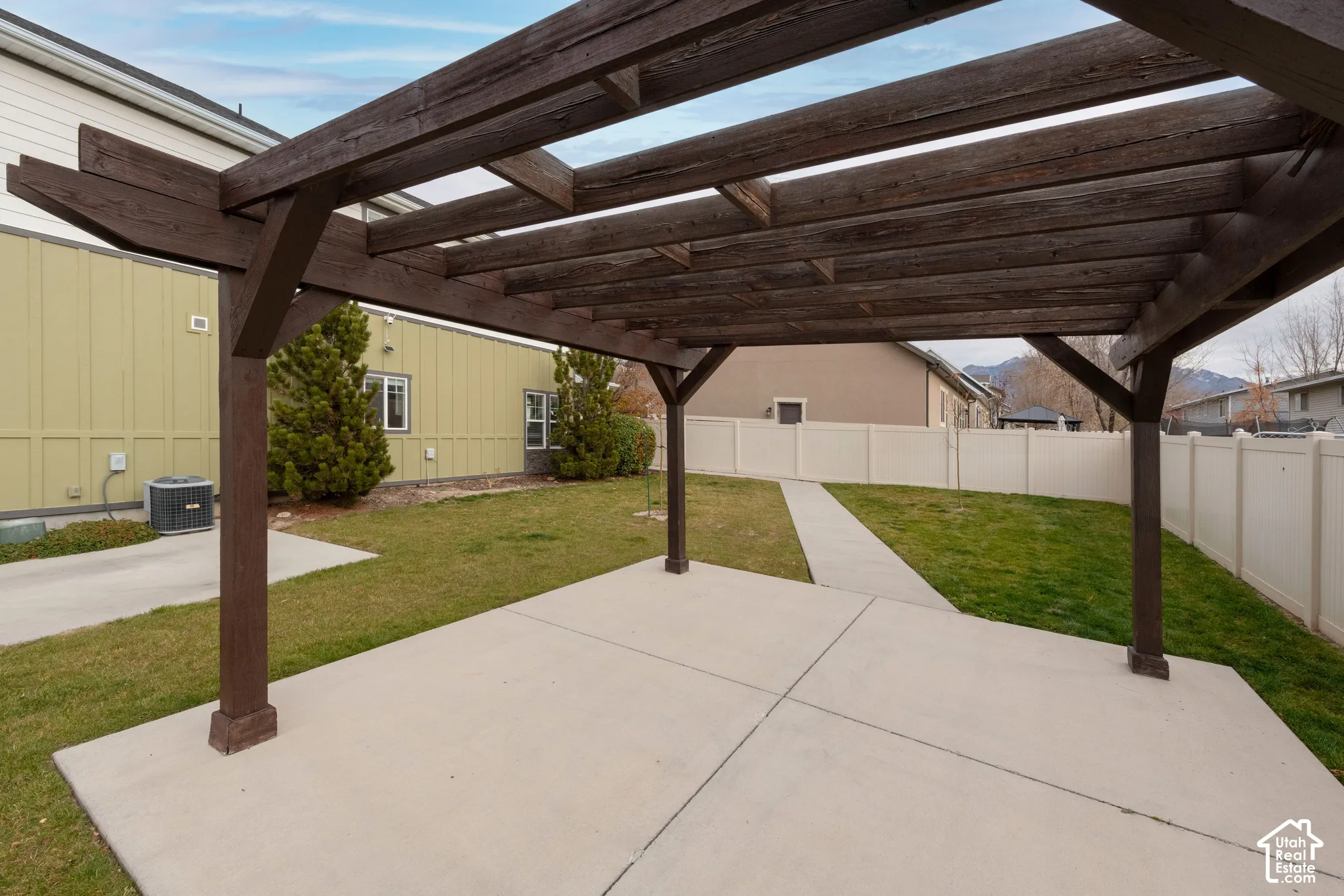 Expansive pergola-covered patio with concrete flooring, a manicured lawn, and perimeter fencing