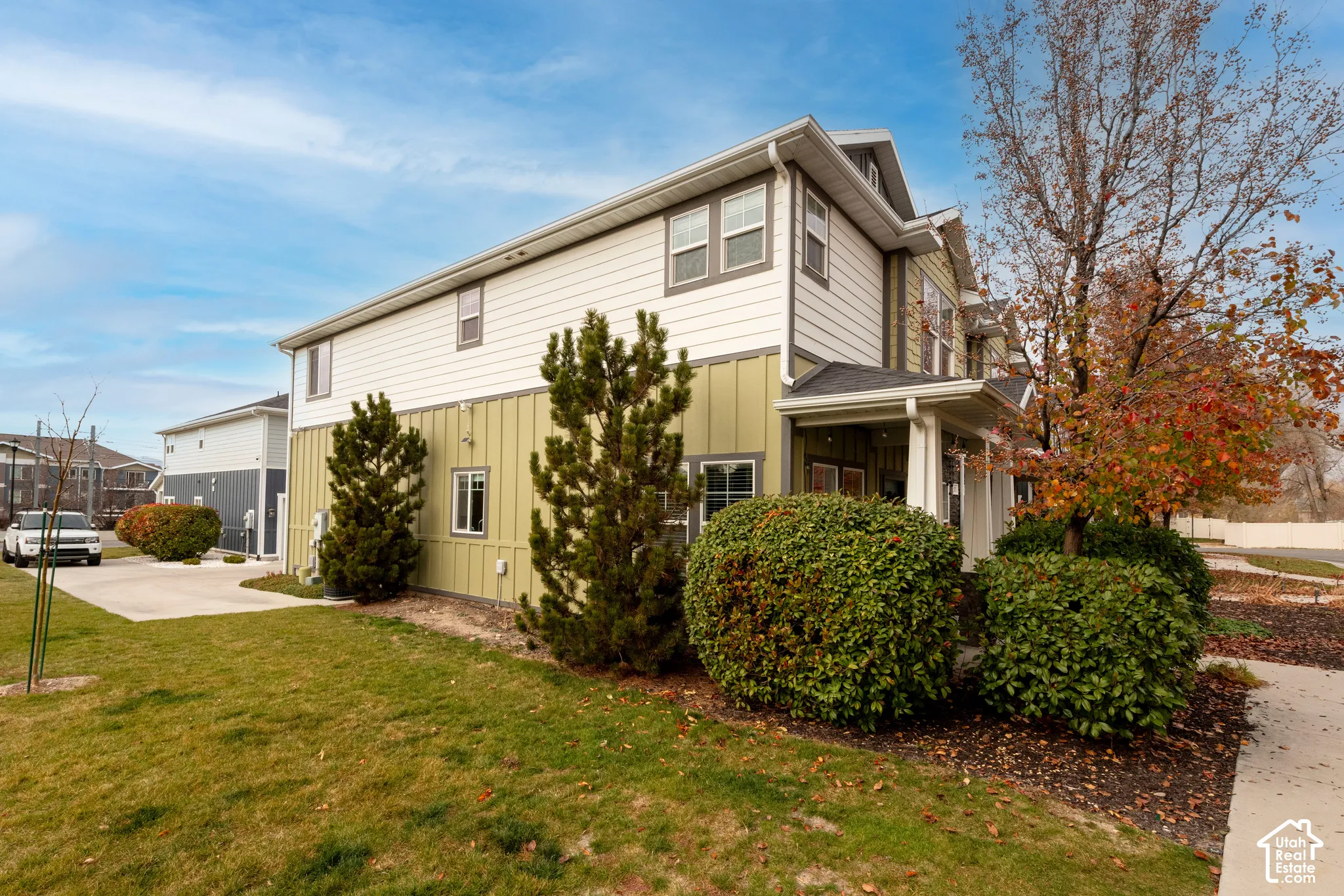 Multi-level exterior with board and batten siding, multiple windows, covered entry, and mature landscaping