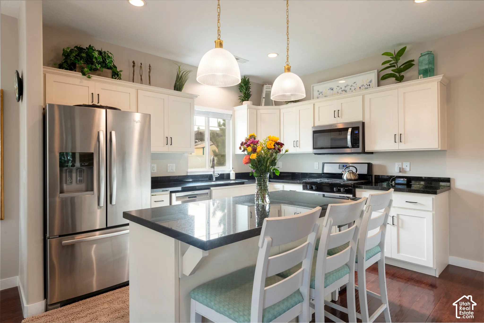 White shaker cabinetry with dark countertops, stainless steel appliances, and a central island with pendant lighting