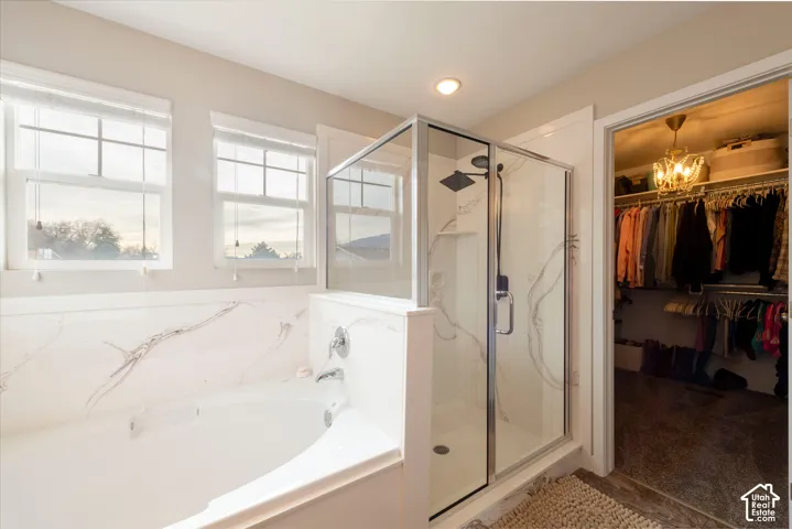 Soaking tub with a polished chrome faucet, glass-enclosed shower with a matte black rainfall showerhead, and a walk-in closet featuring built-in shelving