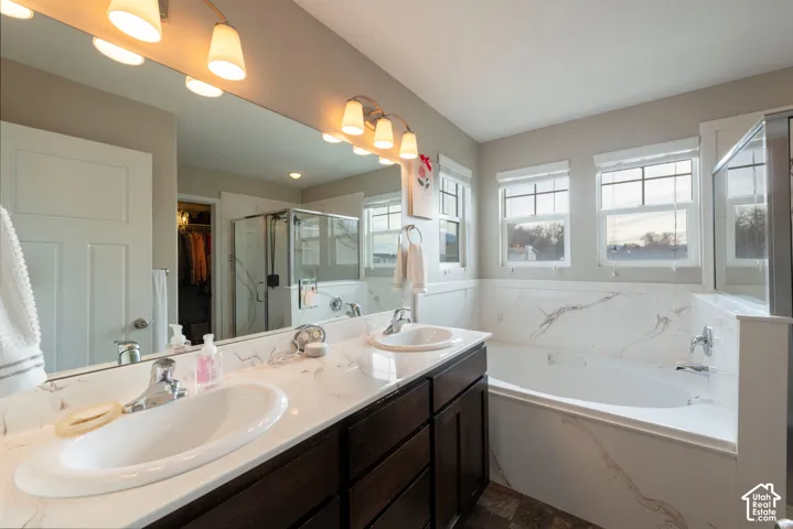 Dual vanity with undermount sinks, spacious mirror, wall-mounted lighting, built-in bathtub with surround, and a glass-enclosed shower