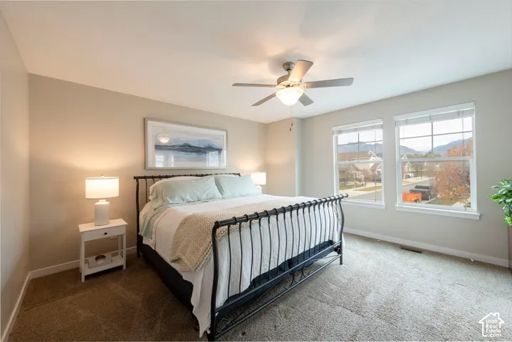 Carpeted bedroom with neutral wall tones, a ceiling fan, and two large windows