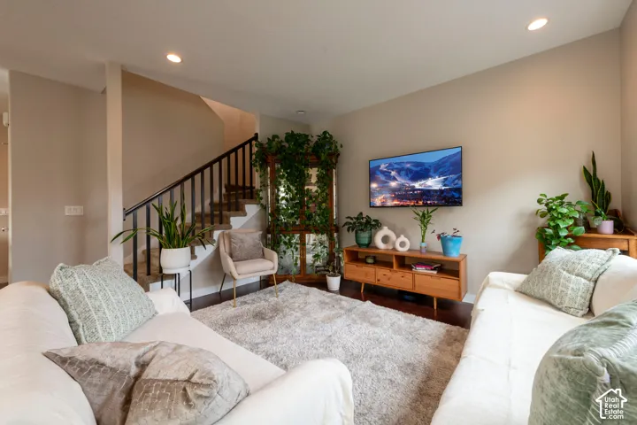 Recessed lighting illuminates the living space featuring wood-finish flooring and a staircase with a black metal railing