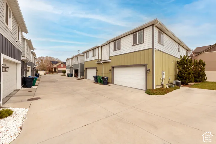 Two-story exterior with horizontal siding and vertical paneling, attached garage, concrete driveway, and established landscape plantings