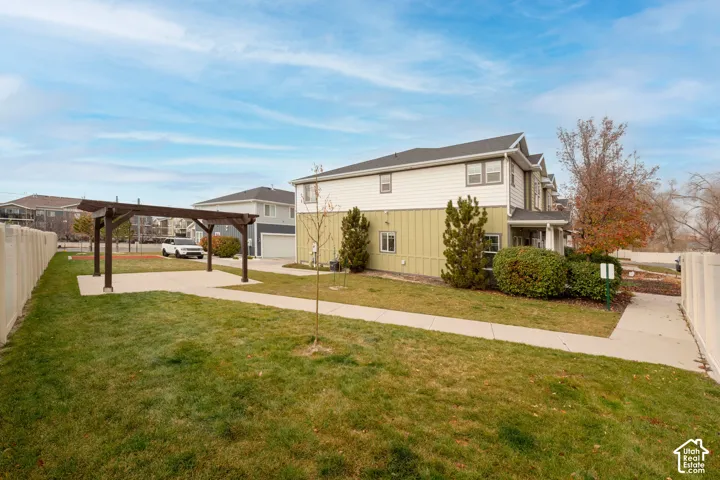 Expansive lawn area with a decorative pergola on a concrete pad, a paved walkway, and a privacy fence