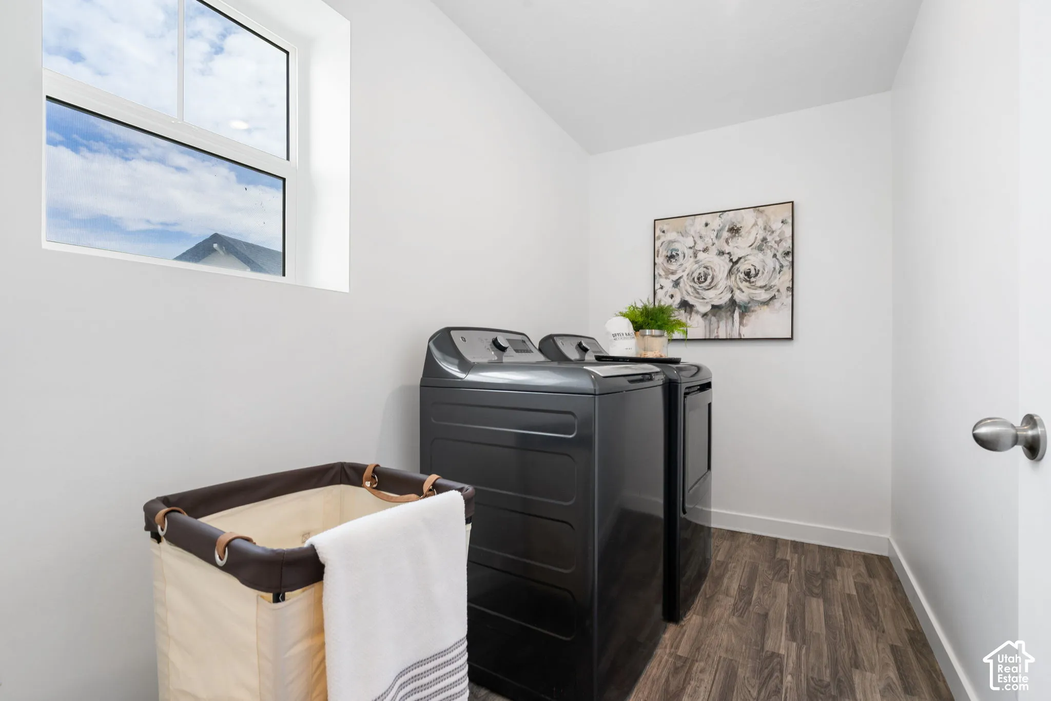 Compact laundry area featuring wood-finish flooring, a white-framed window, and white walls