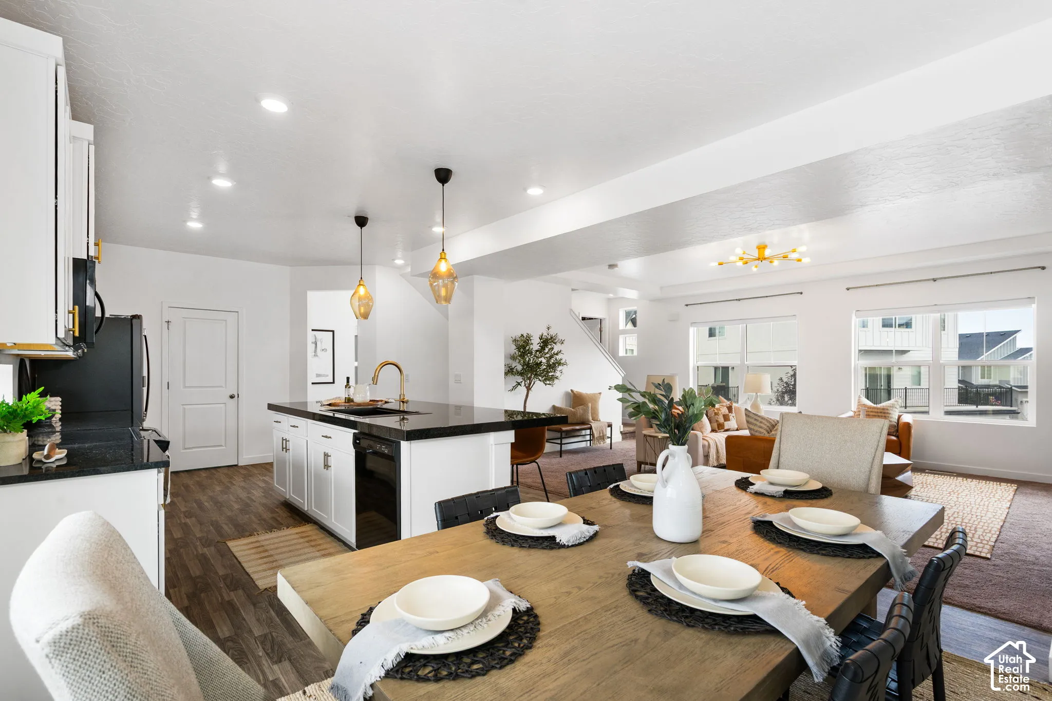 Open-concept living space featuring wood-finish flooring, white cabinetry, dark countertops, and a modern chandelier