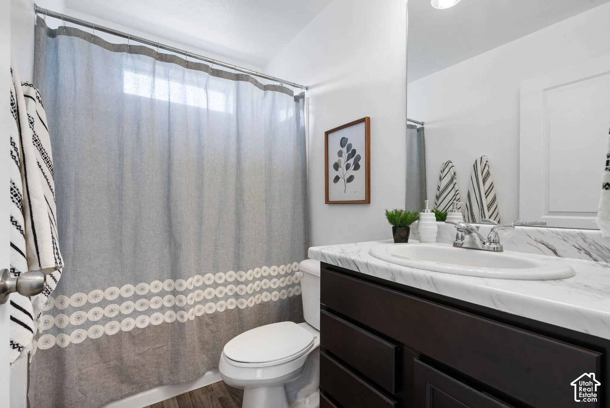 White walls with a window above the shower, dark wood-finish vanity with a white countertop and integrated sink, and an unframed wall mirror