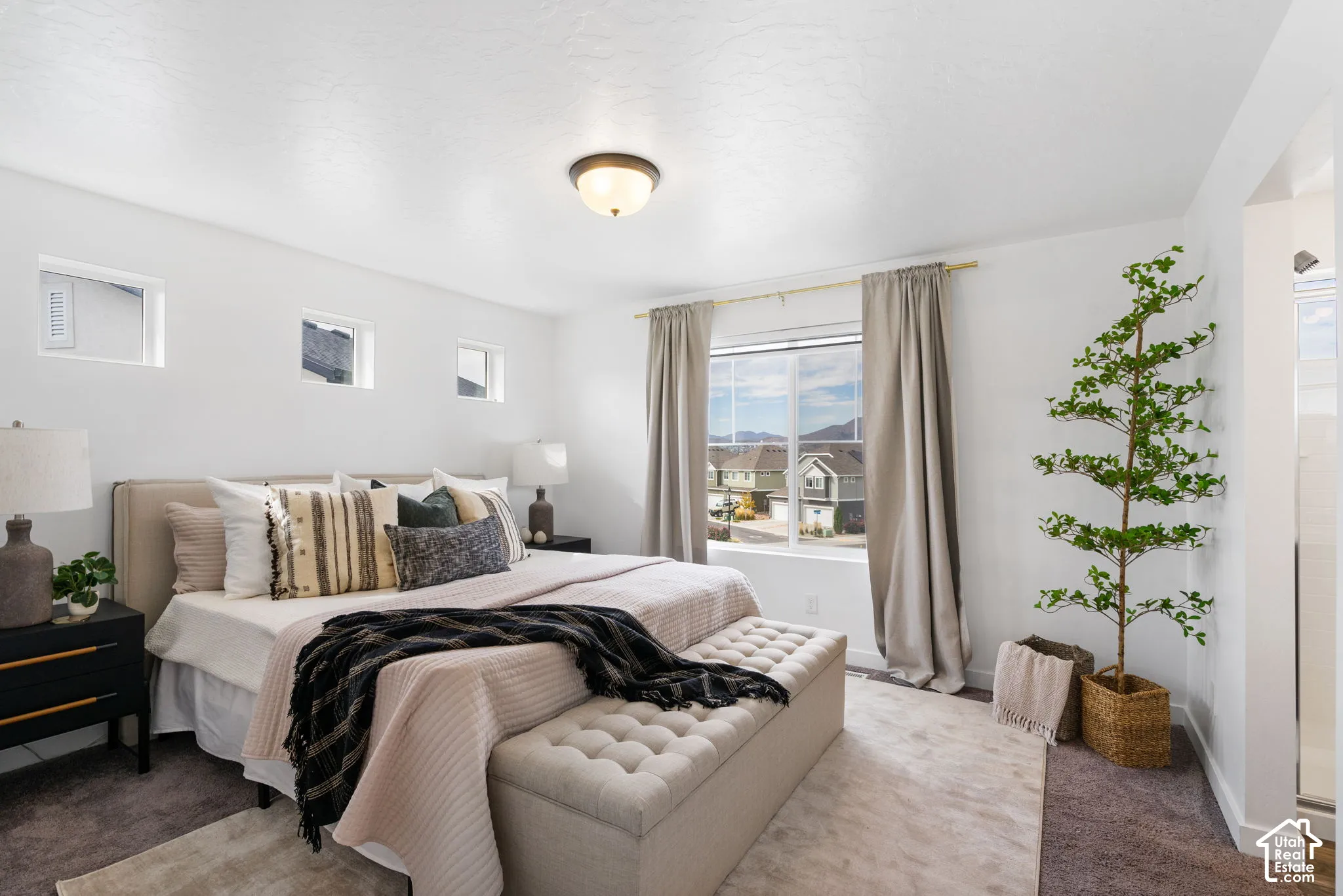 Carpeted flooring, overhead flush mount light, large window with drapes, three high-set windows, white walls