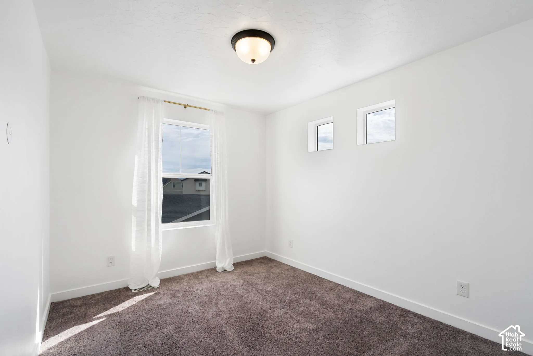Bright interior featuring white walls, carpet flooring, a flush-mount ceiling light, and multiple windows