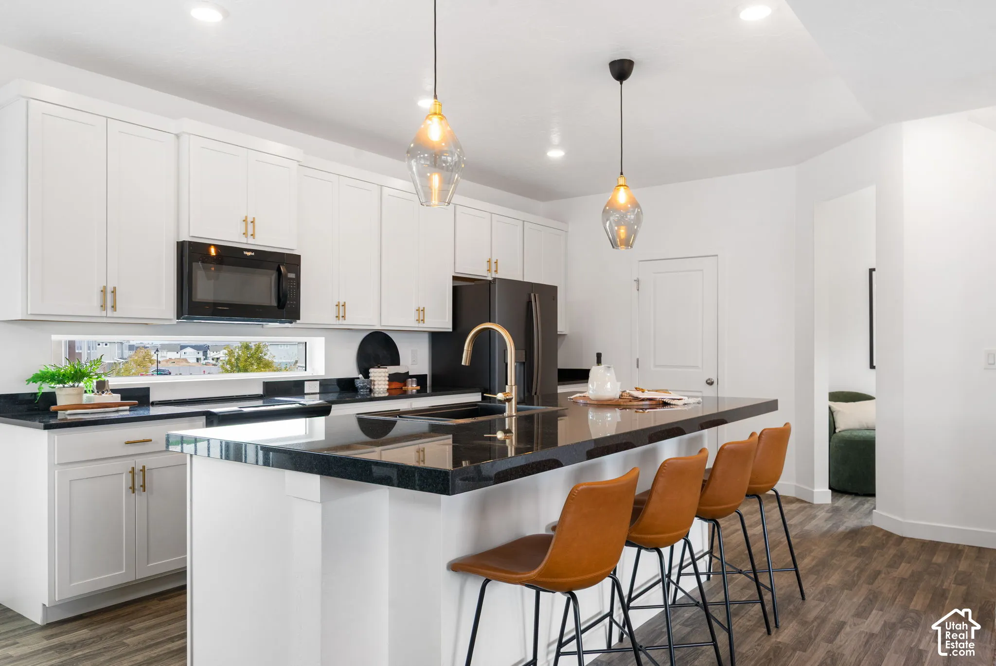 White cabinetry with gold-tone hardware, black countertop surfaces, black appliances, a gold-tone kitchen faucet, and wood-finish flooring