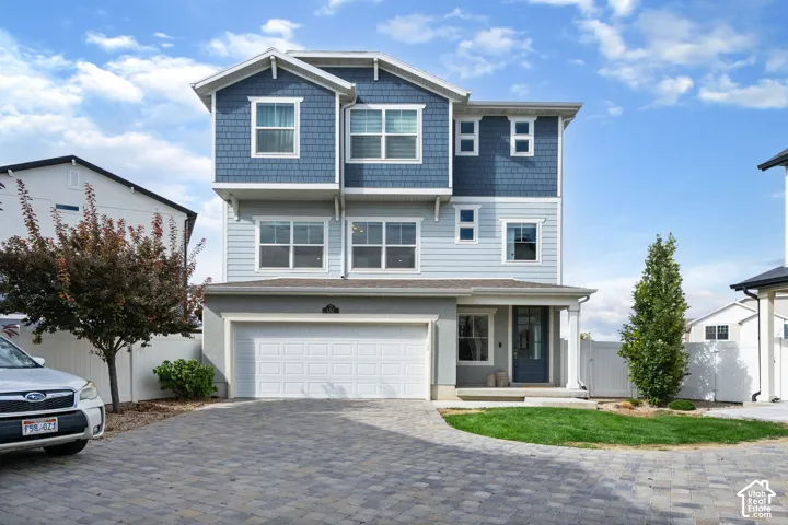 Three-story exterior with multi-tone siding, an attached two-car garage, and a paver driveway