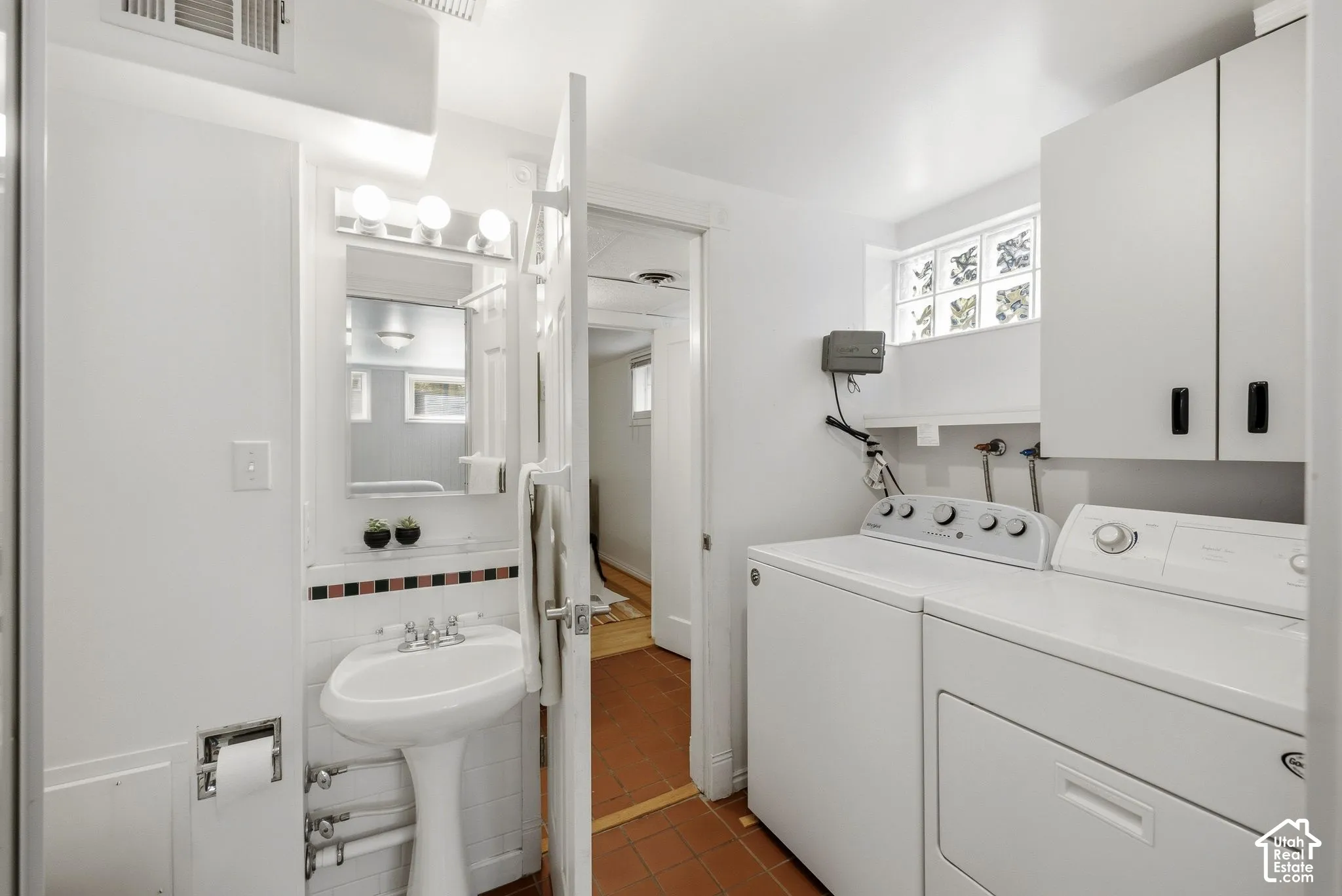 Bathroom and Laundry room. Pedestal sink with chrome faucet, wall-mounted vanity mirror with integrated lighting, laundry appliances, built-in upper cabinetry, and glass block window. Door to Mother in Law appt