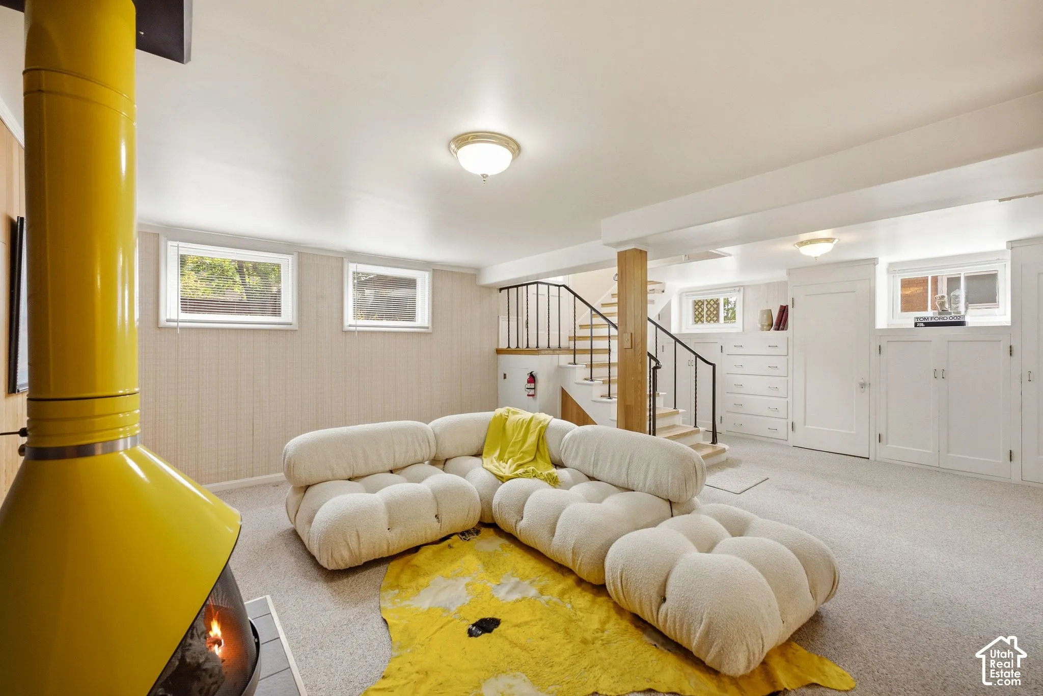 Freestanding yellow fireplace, built-in cabinetry, carpet flooring, and a stairway with black metal railings