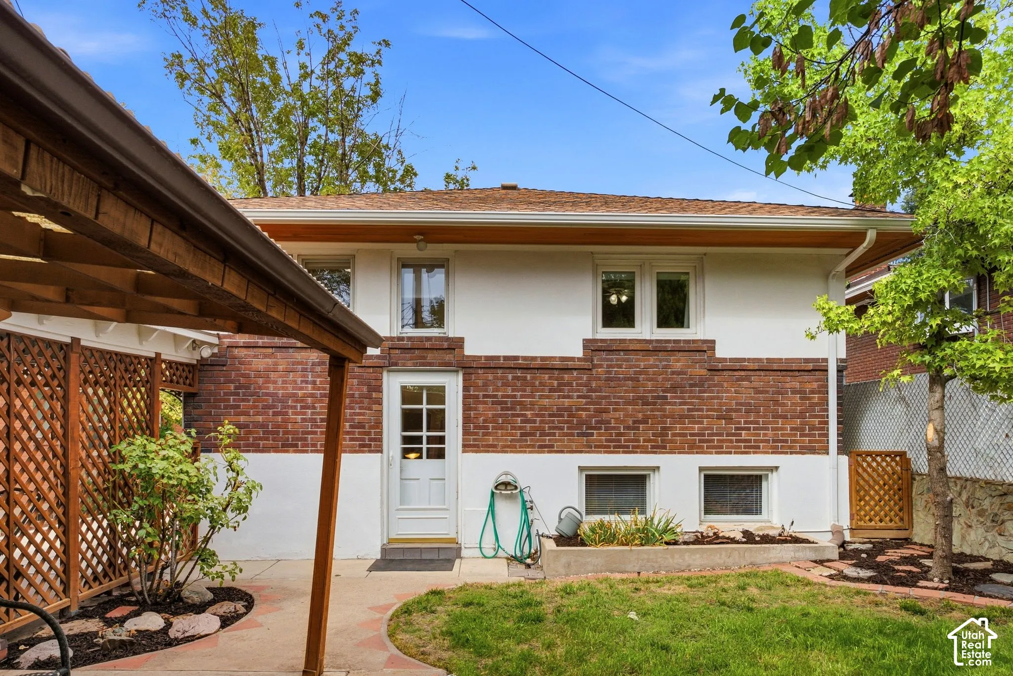 Rear of the house featuring white stucco and brick facade, a covered patio area, and a rear entrance