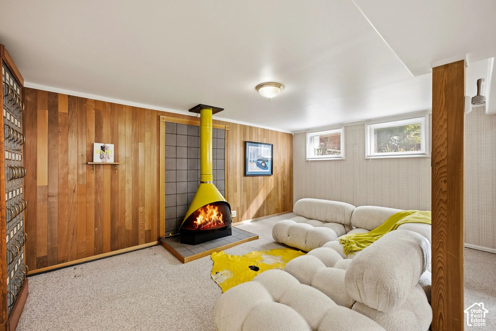 Wood-paneled wall, freestanding fireplace with a tile surround, carpeted flooring.