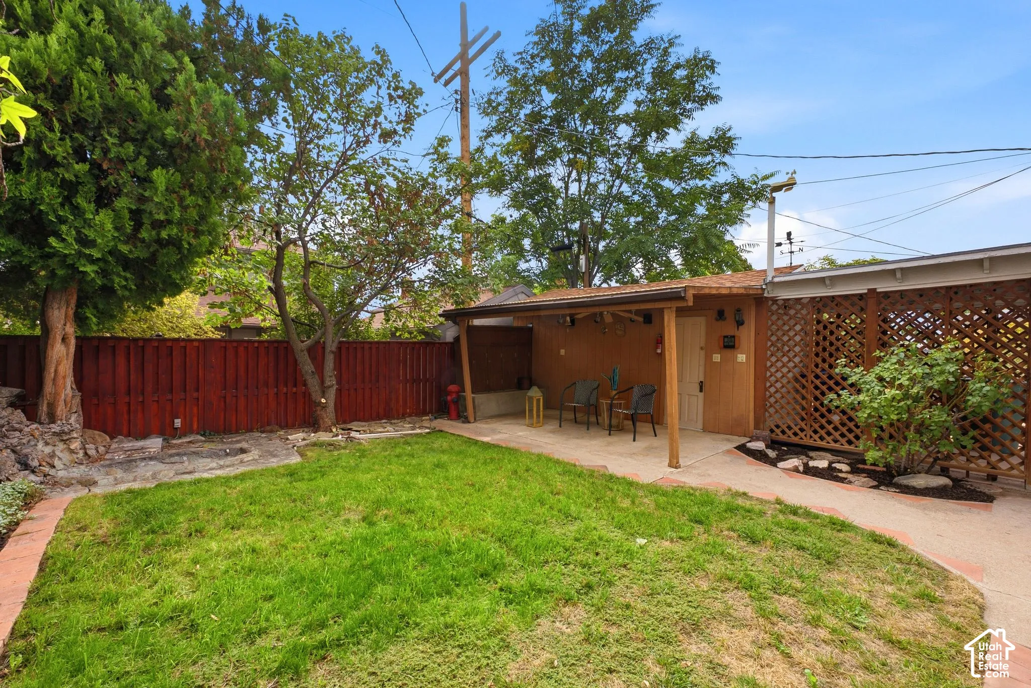 Expansive backyard featuring a covered patio, a privacy lattice fence, a manicured lawn, and mature trees