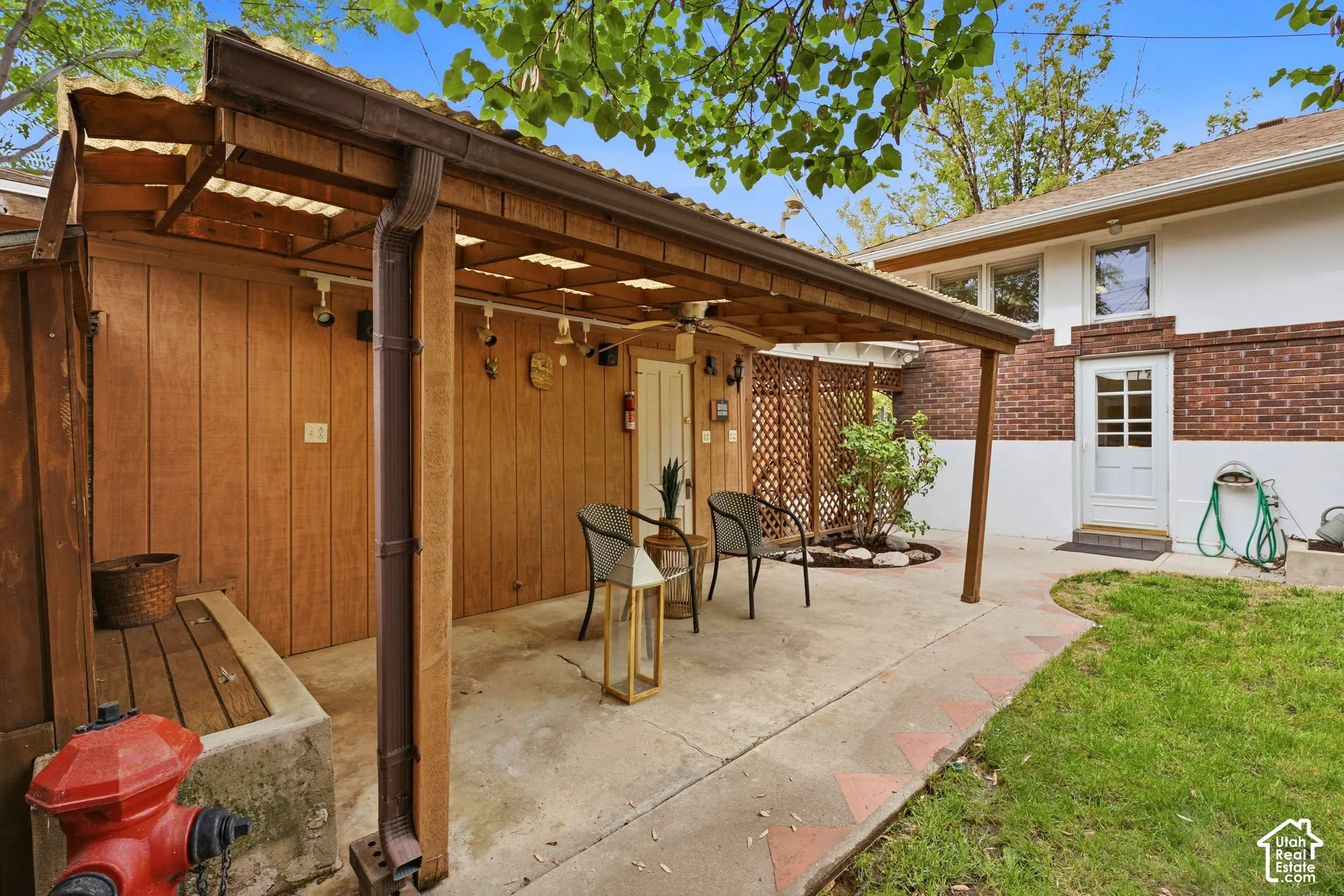 Covered patio area, solid wood paneling, lattice privacy screen, concrete patio, and a grass lawn