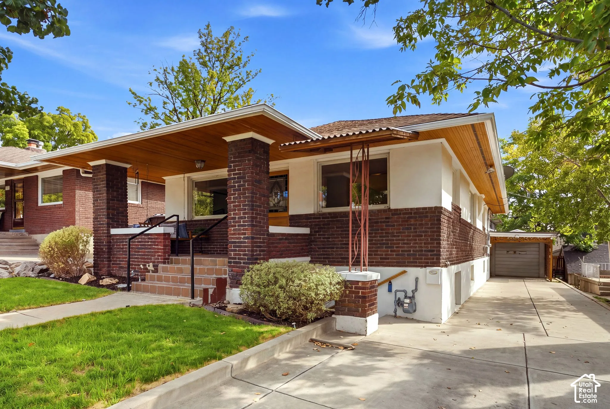 Brick and stucco exterior with a wood-paneled porch ceiling, covered front entry, and a paved driveway leading to a detached garage