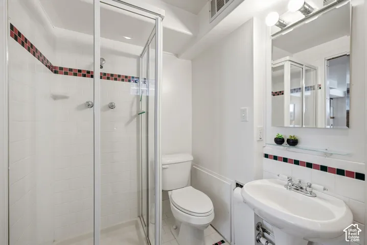 Pedestal sink with chrome fixtures, mirrored medicine cabinet, and a glass-enclosed shower with subway tile surround and decorative tile accent