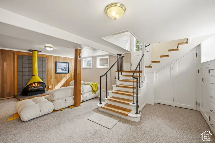 Wood-paneled wall with a modern freestanding fireplace, carpeted flooring, and a staircase with wood treads and a black metal railing. Extensive storage
