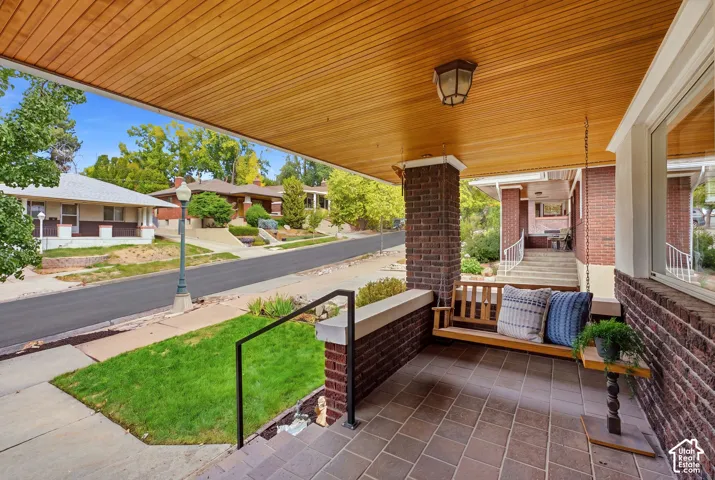 Covered front porch featuring a wood-finish ceiling, brick columns, and a tile floor