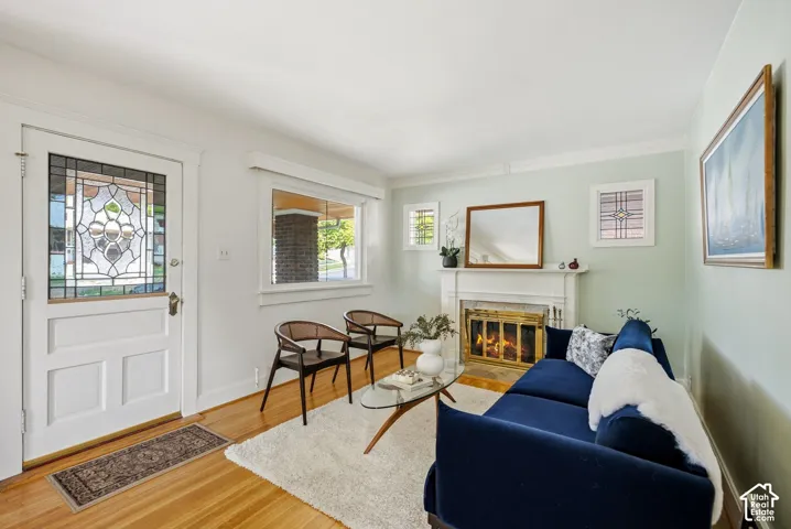 Hardwood flooring, decorative stained glass entry door, fireplace with brass firebox, white mantel, and crown molding