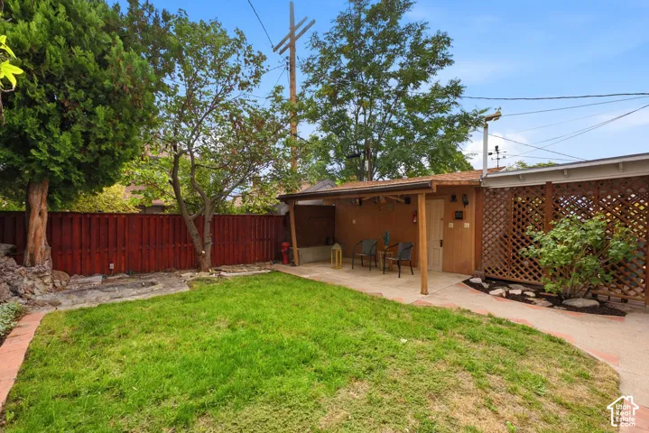 Expansive backyard featuring a covered patio, a privacy lattice fence, a manicured lawn, and mature trees