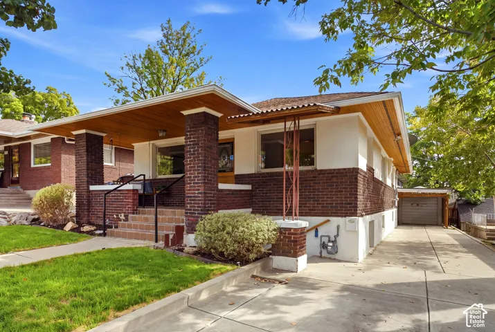 Brick and stucco exterior with a wood-paneled porch ceiling, covered front entry, and a paved driveway leading to a detached garage