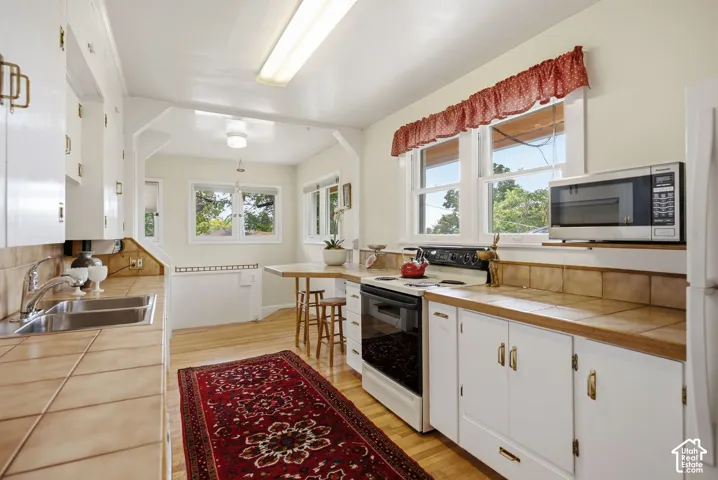 White cabinetry with brass-tone hardware, tile countertops, stainless steel double basin sink, and hardwod flooring