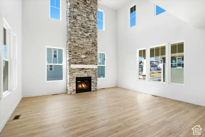 Vaulted ceilings, a stacked stone fireplace with a white mantel, wood-finish flooring, and multiple windows
