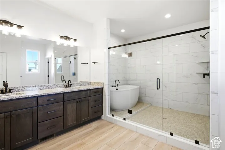 Double vanity with a speckled countertop, a large mirror, a separate glass-enclosed shower, a freestanding soaking tub, and tile flooring