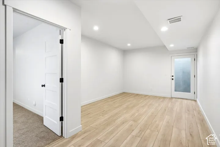 Recessed lighting, light wood-finish flooring, white walls, white solid core door with matte black hardware, and an exterior door with frosted glass