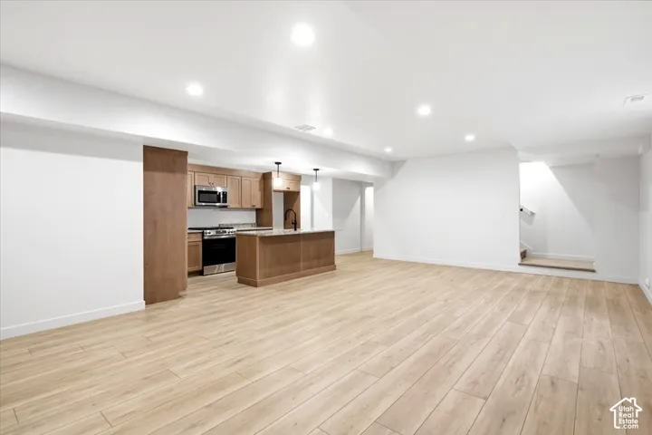 Spacious open-concept area featuring wood-finish flooring, recessed lighting, and a kitchen with warm-toned cabinetry, stainless steel appliances, and a central island