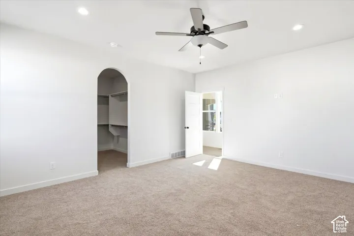 Recessed ceiling lighting, ceiling fan, neutral carpeting, arched doorway, and built-in closet shelving